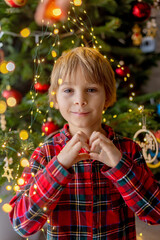Sweet blond child, cute boy, decorating christmas tree at home in pyjamas