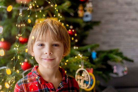 Sweet blond child, cute boy, decorating christmas tree at home in pyjamas