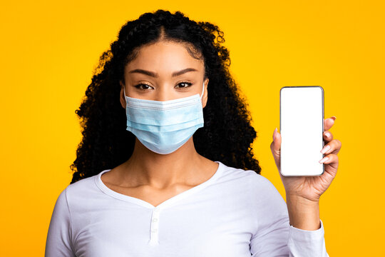 Coronavirus Map App. Young black woman wearing protective medical face mask showing smartphone with blank white screen, demonstrating copy space for virus outbreak tracking application design, mockup