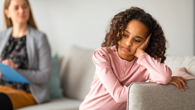 Mental health of child in adolescence. Sad girl sitting back to doctor, young professional psychologist talking with teenager. Specialist consulting teen at counselling therapy session