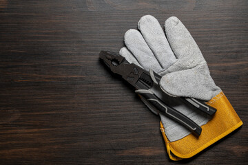 Metal pliers and leather safety gloves on wooden table, top view, copy space, closeup