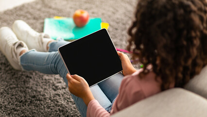 African american curly schoolgirl using digital tablet with blank screen, using mobile application...