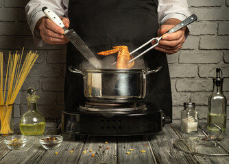 A chef skillfully maneuvers tongs and a knife while cooking chicken in a pot on a stovetop. Fresh...