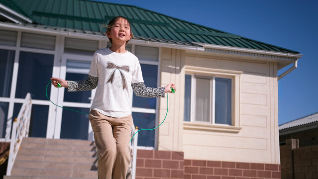 Physical education. A young girl jumps rope in the yard of her house. A teenager is having fun doing his favorite outdoor activity