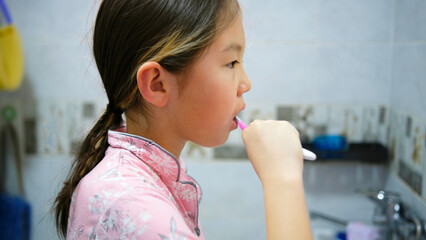 Sleepy Asian girl is busily brushing her teeth in the bathroom, profile view. Oral care. Morning hygiene. The schoolgirl