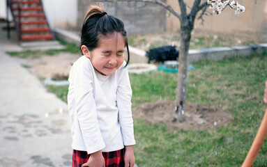 Fototapeta premium A young girl stands in the rain and looks happy. An Asian small child is hosed down with water. Summer fun. Children's simple games