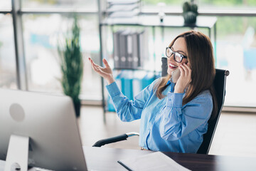 Young assistant woman speaking on mobile phone and working at desk in modern office environment