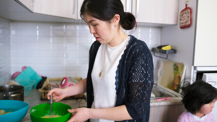 Mom is working in the kitchen. A woman prepares dough for pancakes. Household chores. She's wearing...