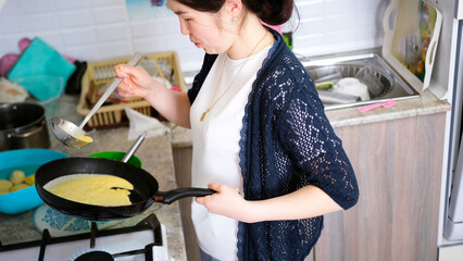 An Asian woman cooks pancakes in a frying pan on a gas stove. Mom bakes delicious pancakes for tea....