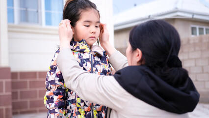 A mother comforts her little daughter. A woman adjusts the hair of a little Asian girl. Caring and...