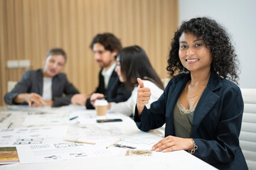 African businesswoman giving a thumbs up while her colleagues sitting and having a meeting in the background