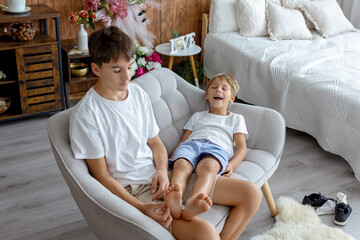 Happy positive children, tickling on the feet, having fun together, boy brothers having wonderful...