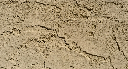 A textured beige surface with deep crevices, illuminated by sunlight, casting shadows to accentuate the roughness and depth of the material, offering a tactile and organic visual experience.