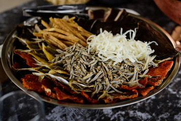 A close-up of a rustic metal platter generously loaded with an assortment of savory beer snacks, including dried fish, jerky, and string cheese.
