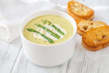 Creamy asparagus soup in white bowl with swirl and toasted ciabatta