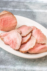 Perfectly sliced roast beef medium rare with seared crust on white plate