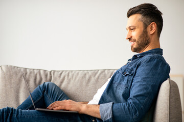 Smiling middle-aged man using modern laptop, having part-time job at home, copy space. Happy...