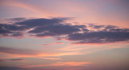Fototapeta premium A pastel sunset sky showcases a band of dark gray clouds subtly illuminated with peach and lavender hues, against a backdrop of lighter, almost translucent clouds and a soft orange horizon