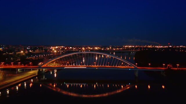Beautiful arched Appolo Bridge with switched on illumination. Drone footage over the waterscape of the Danube at night.