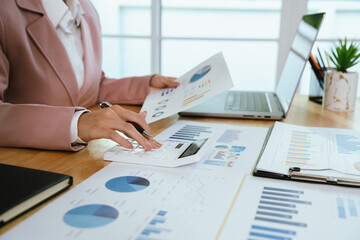A business professional analyzing financial charts and graphs with a pen, calculator, and laptop,...
