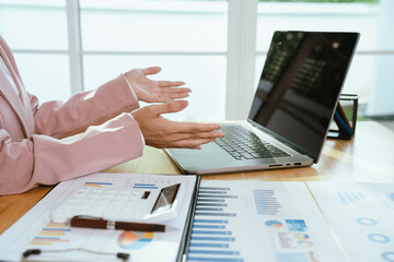 A business professional analyzing financial charts and graphs with a pen, calculator, and laptop,...