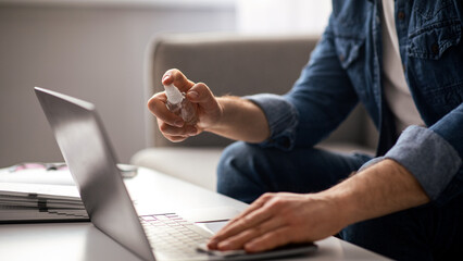 Closeup of male hand using disinfectant spray and cloth for cleaning laptop keyboard while working...