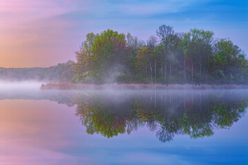 Spring landscape at dawn of the shoreline of Whitford Lake, with mirrored reflections in calm water, Fort Custer State Park, Michigan, USA