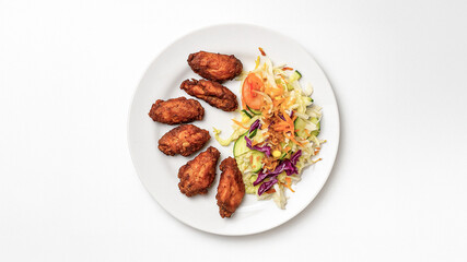 Top view of a white plate with crispy fried chicken wings and fresh vegetable salad on a white background. The image is isolated, clean, and perfect for menu design, advertising, or food blog.