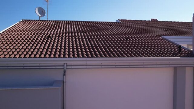 A plumber installed aluminum gutters and aluminum-colored downspouts on a newly built home with a tile roof. The areas of the roof without gutters were finished with aluminum cornice trim.