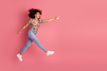 Joyful young woman in casual floral blouse posing energetically on pink background, showcasing vibrant youthfulness