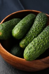 Fresh cucumbers in bowl on dark textured table, closeup