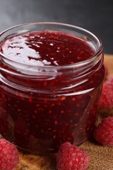 Sweet raspberry jam in glass jar and berries on table, closeup