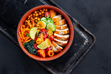 Buddha bowl with baked chicken breast, chickpeas and fresh vegetables on a black background top view copy space for text
