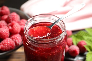 Delicious raspberry jam in glass jar and spoon on table, closeup