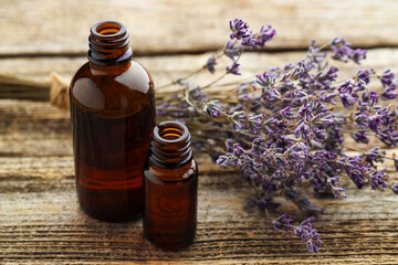 Lavender essential oil in bottles with flowers on wooden table, closeup
