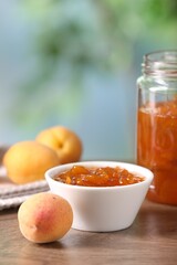 Tasty apricot jam and fresh fruits on wooden table against blurred background, closeup
