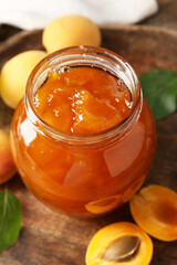 Tasty apricot jam and fresh fruits on wooden table, closeup