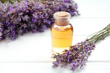 Lavender essential oil and flowers on white wooden table, closeup