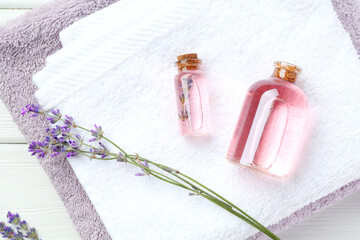 Lavender essential oil, flowers and towels on white wooden table, flat lay