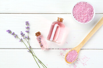 Lavender essential oil, flowers and sea salt on white wooden table, flat lay