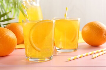 Refreshing soda water with orange slices in glasses, jug and fresh fruits on pink wooden table,...
