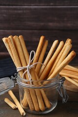 Delicious grissini sticks in open glass jar on wooden table, closeup