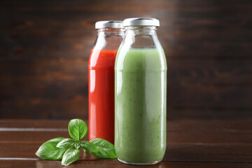 Tasty juices in glass bottles and basil on wooden table