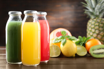 Tasty juices in glass bottles, fresh fruits, mint and basil on wooden table, selective focus