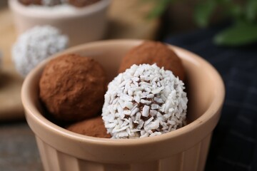 Delicious homemade candies with cocoa powder and coconut flakes in bowl on table, closeup