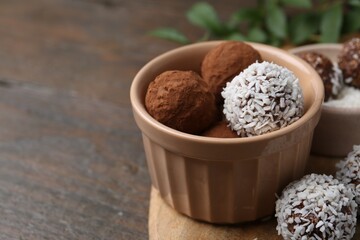 Delicious homemade candies with cocoa powder and coconut flakes in bowl on wooden table, closeup....