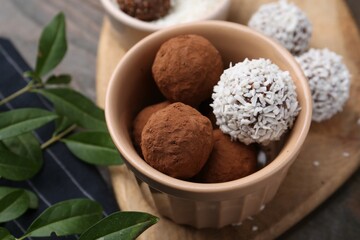 Delicious homemade candies with cocoa powder, coconut flakes and green leaves on table, closeup