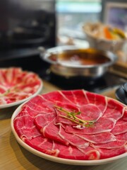 Thinly sliced raw beef arranged on a plate for hot pot / shabu-shabu, with simmering broth in the background
