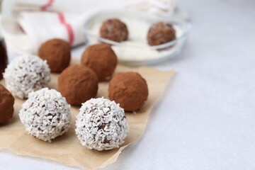Delicious homemade candies with cocoa powder and coconut flakes on light table, closeup. Space for text