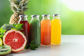 Tasty juices in glass bottles, fresh ingredients and mint on white table against blurred green...